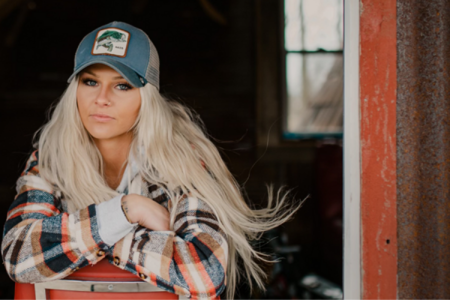 A woman wearing a hat and plaid shirt is leaning on a red chair.