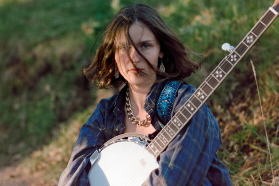 A woman is sitting in the grass holding a banjo