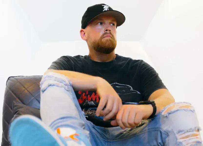 A man with a beard is sitting on a bean bag chair holding a remote control.