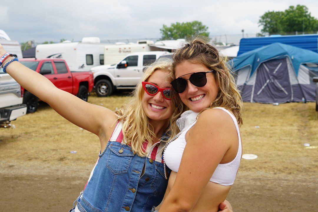 Two women are posing for a picture in a field with tents in the background.