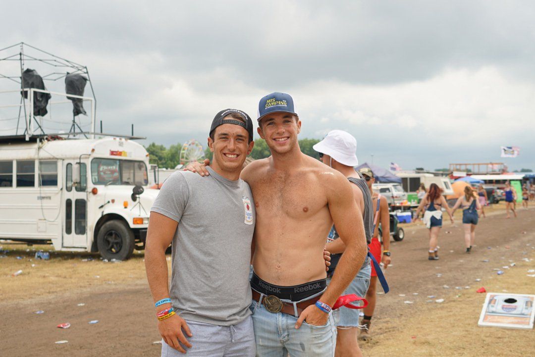 Two shirtless men are posing for a picture in front of a white bus.