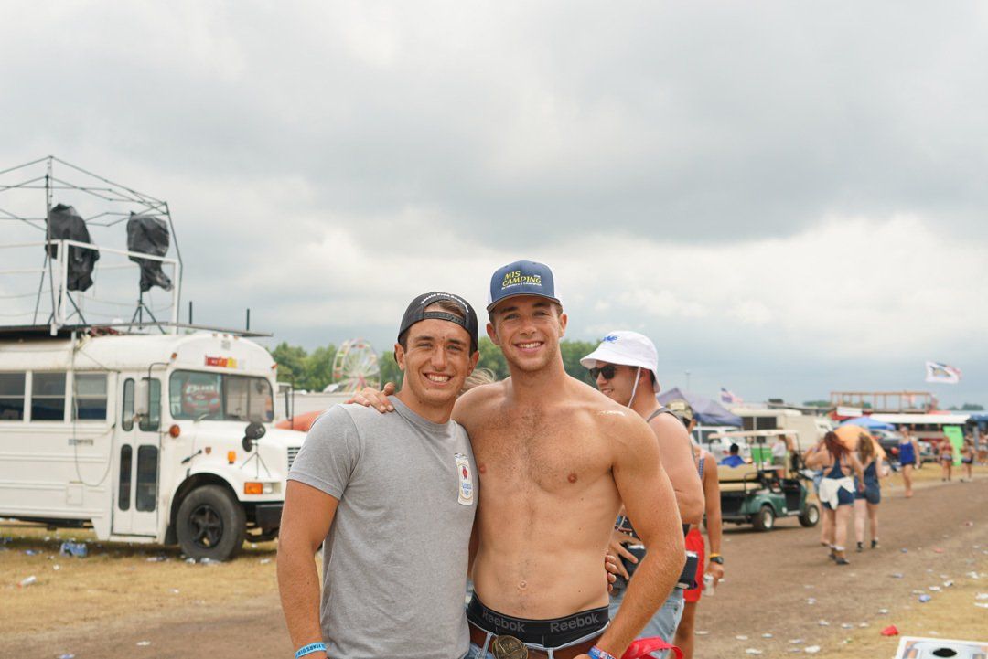 Two shirtless men are posing for a picture in front of a white bus.  Wilder Boys