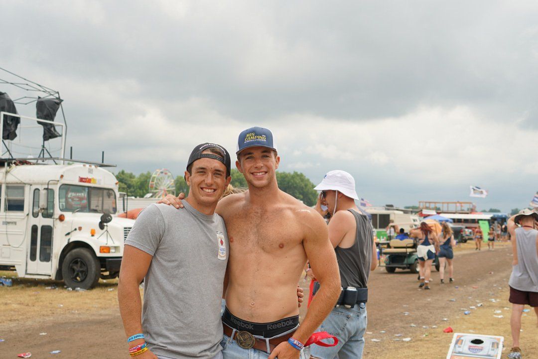 Two shirtless men are posing for a picture in front of a bus