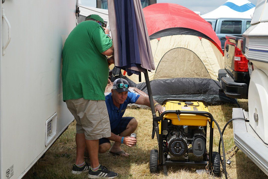 Two men are working on a generator in front of a tent.