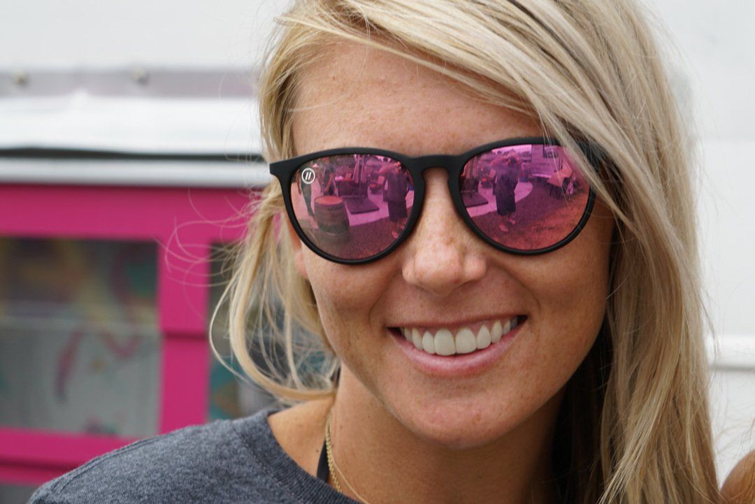 A close up of a woman wearing sunglasses and smiling.