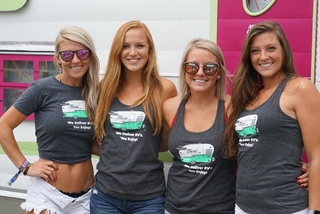Four women are posing for a picture in front of a pink trailer.
