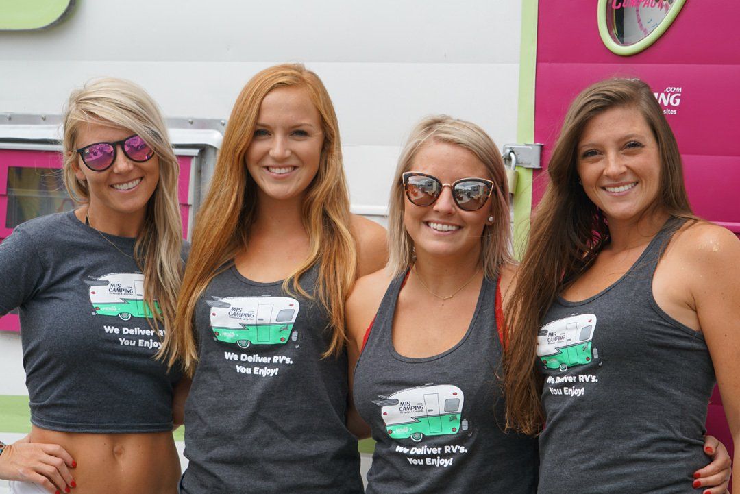 Four women are posing for a picture in front of a trailer.