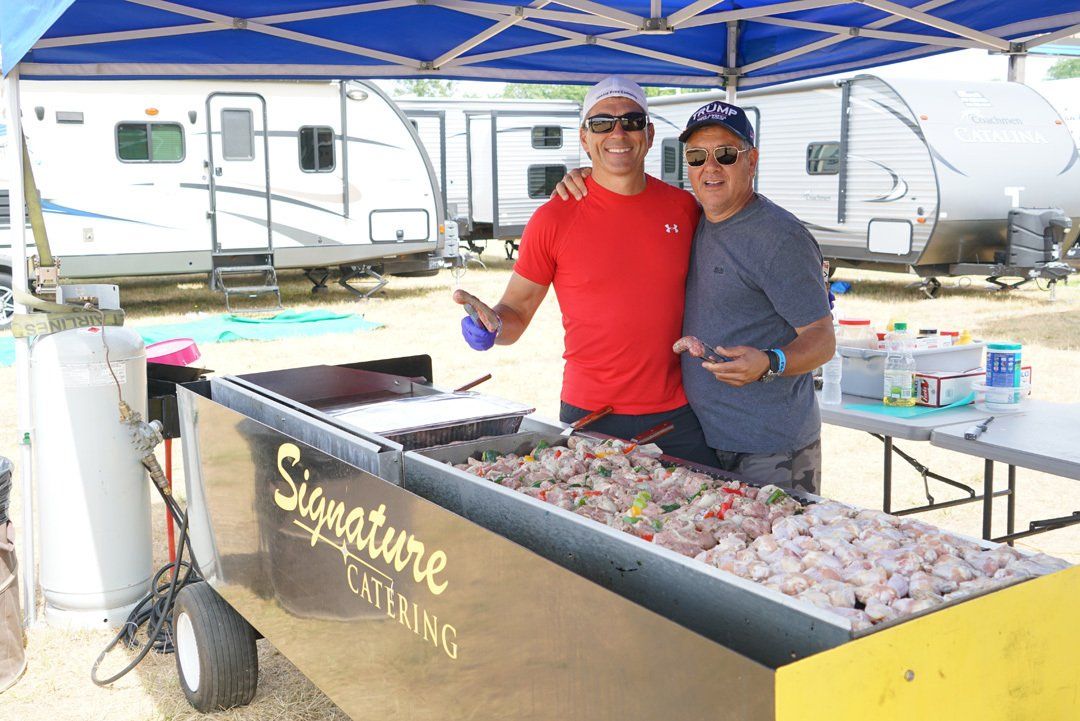 Two men are standing in front of a signature catering cart.