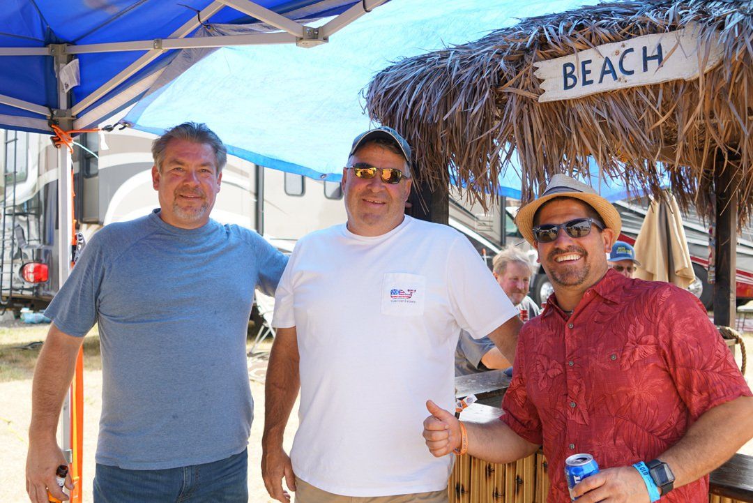 Three men are posing for a picture in front of a beach sign.