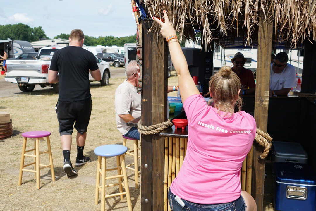 A woman in a pink shirt is standing in front of a thatched hut.