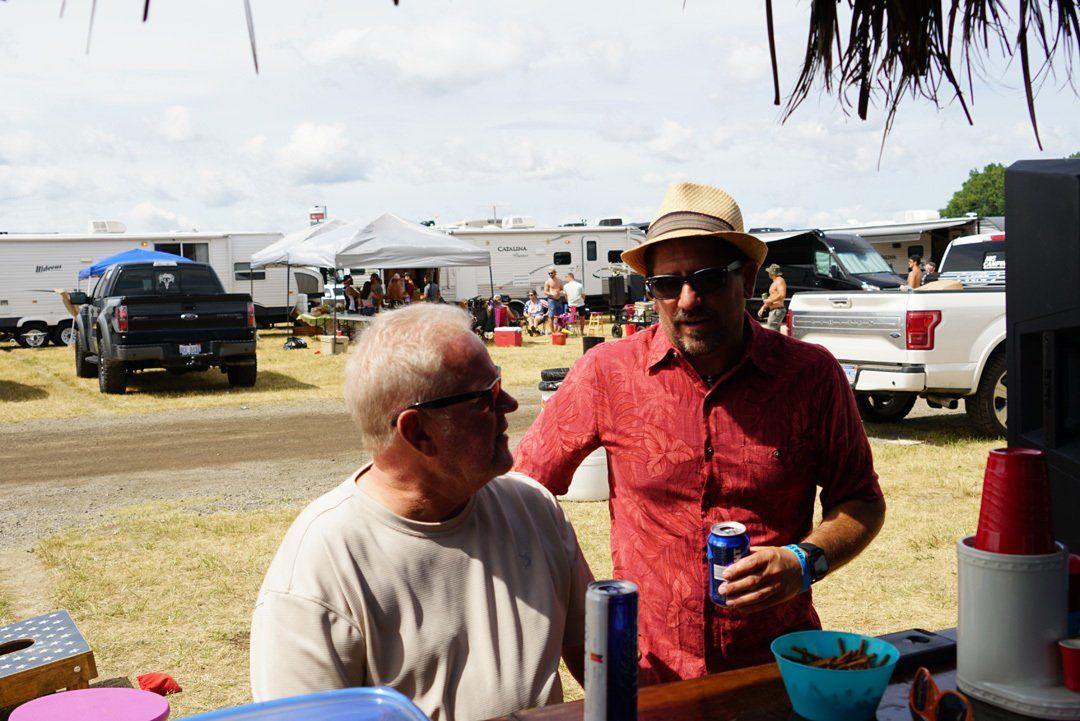 Two men are standing next to each other in a field holding cans of red bull.