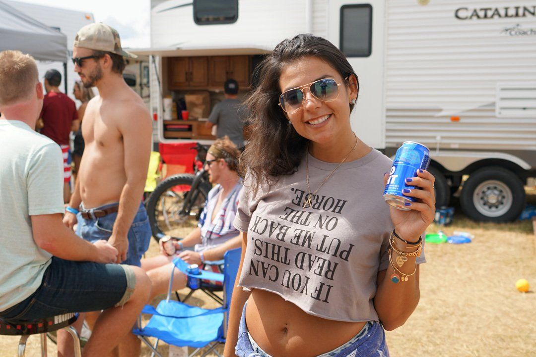 A woman in a crop top is holding a can of beer.