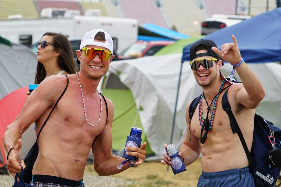 Two shirtless men are standing next to each other in front of a tent.