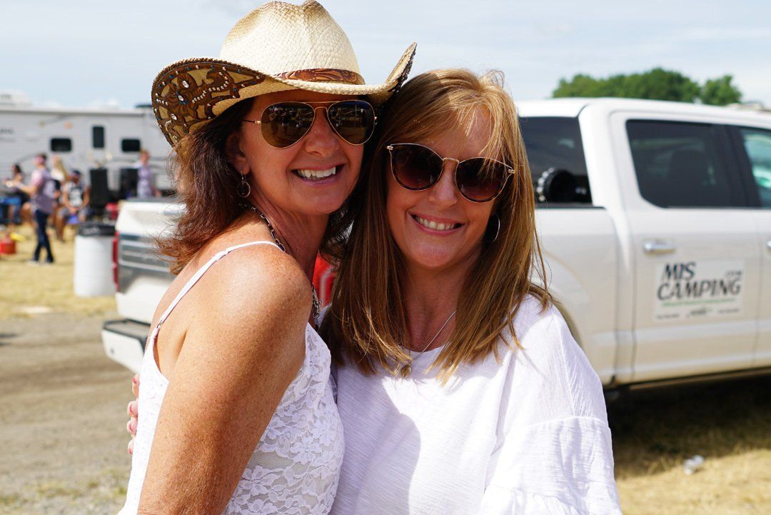 Two women wearing cowboy hats and sunglasses are posing for a picture in front of a white truck.