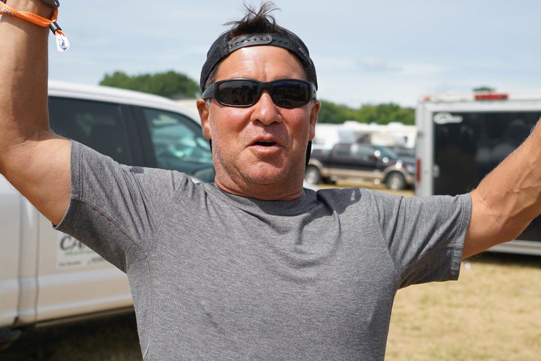 A man wearing sunglasses and a hat is raising his arms in the air.