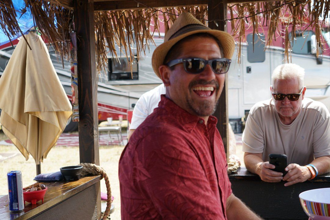 A man wearing a hat and sunglasses is smiling while sitting at a table.