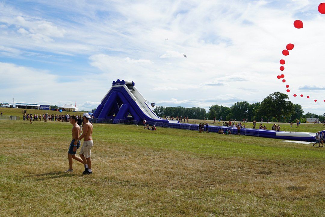 A couple walking in a field with a large inflatable slide in the background