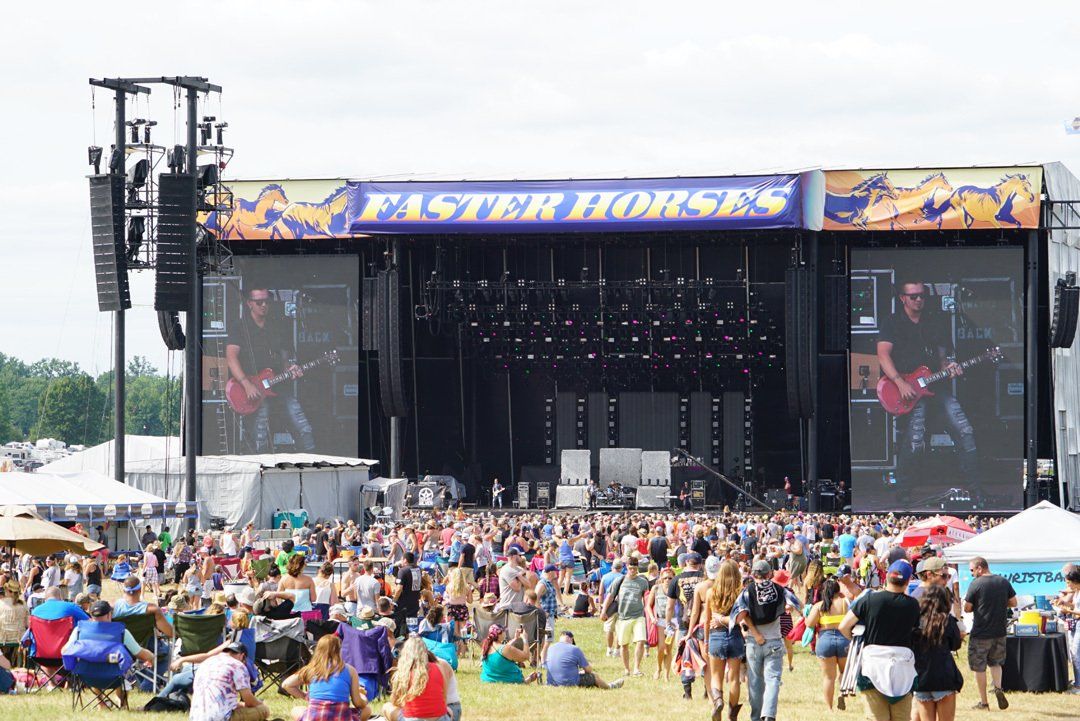A large crowd of people are gathered in front of a large stage at a music festival.