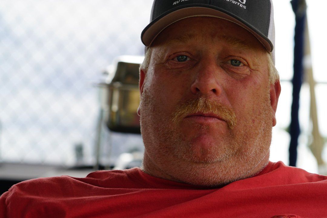 A man wearing a hat and a red shirt is looking at the camera.