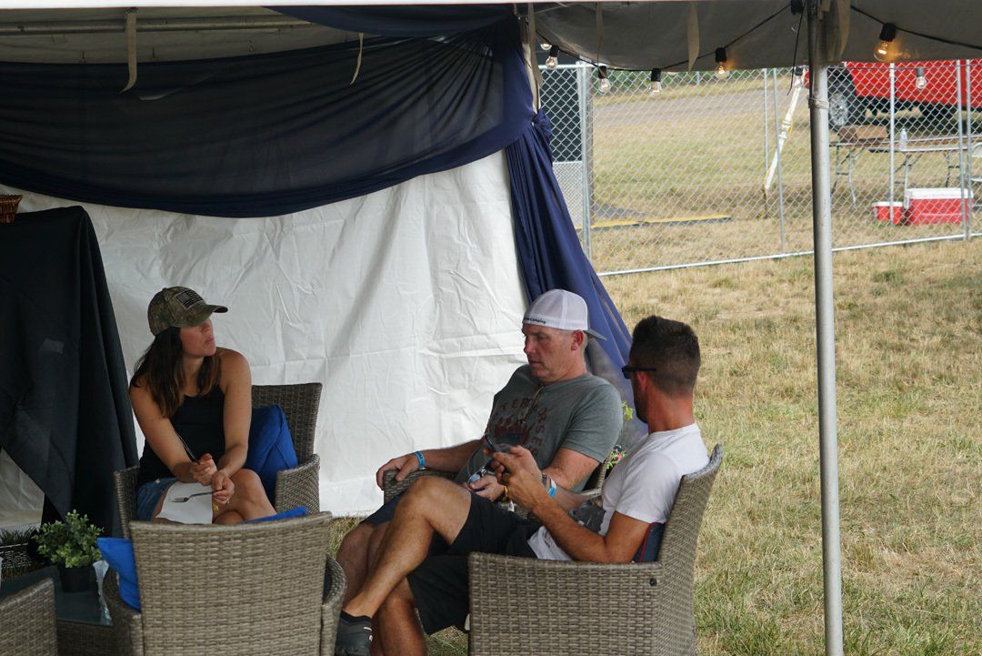 A group of people are sitting under a tent in a field.