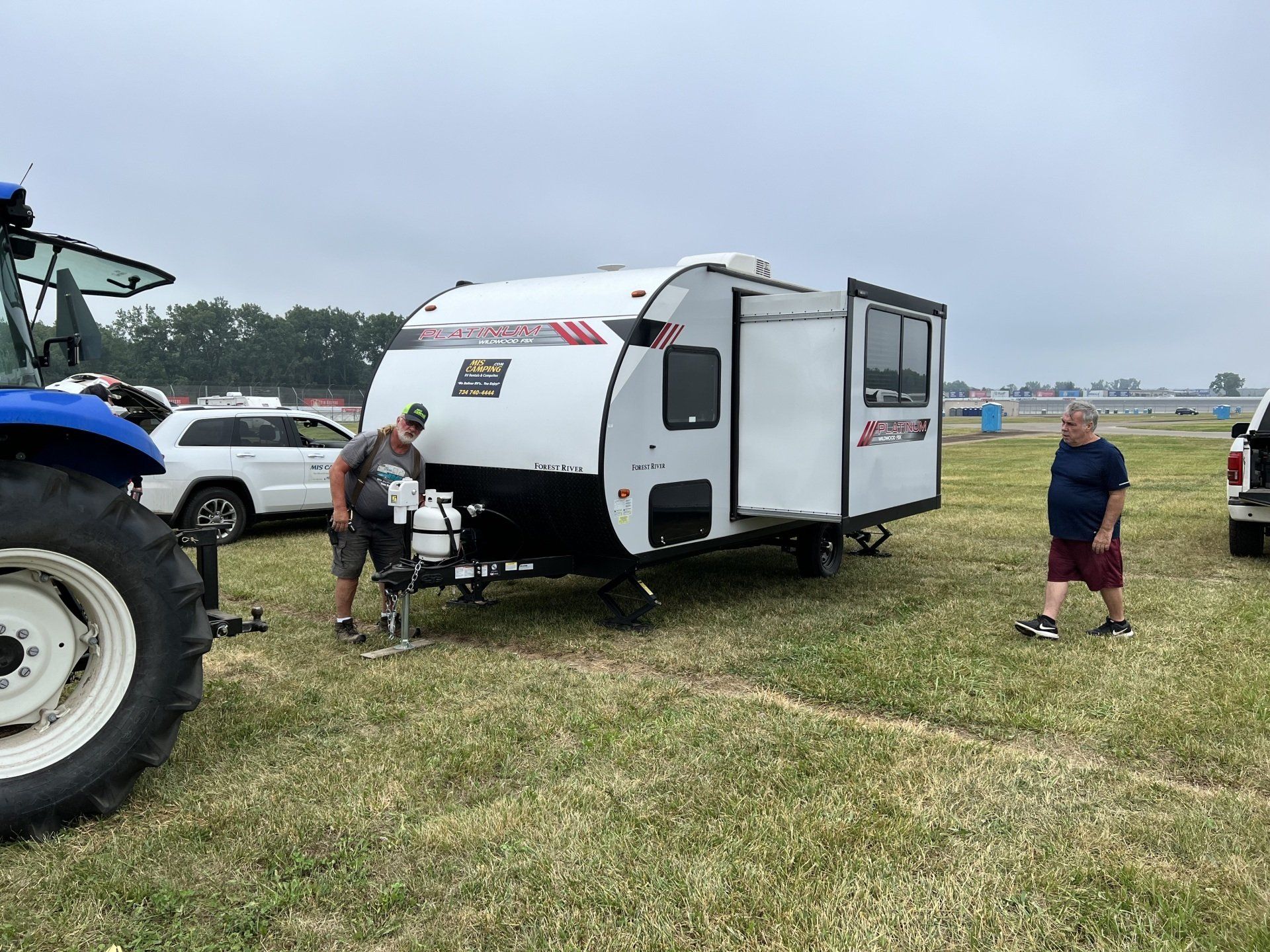 Two men are standing next to a trailer in a grassy field.
