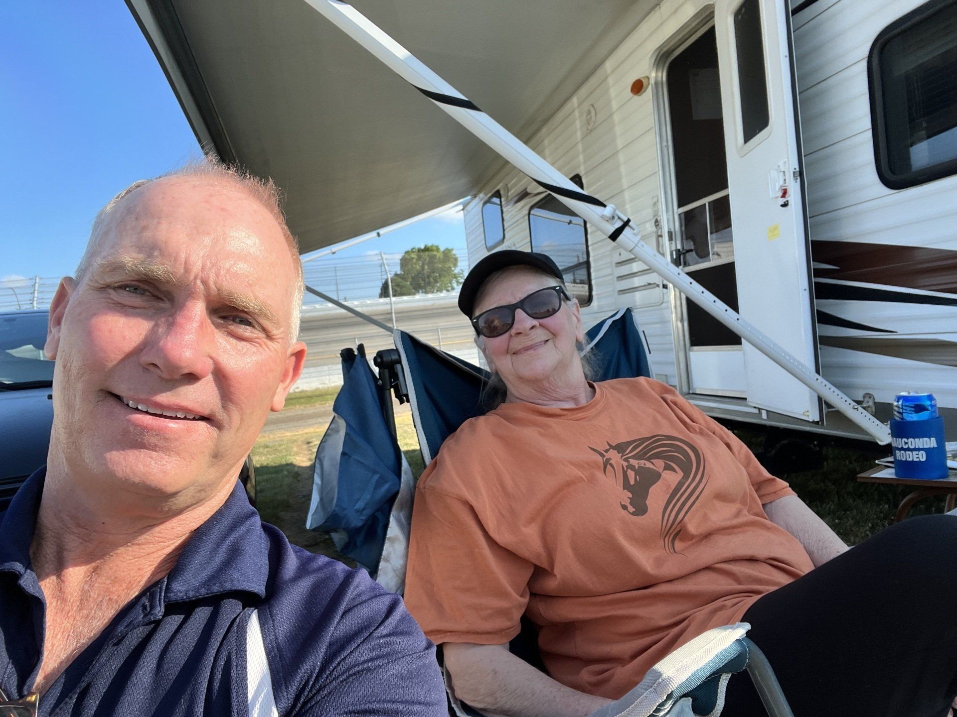 A man and a woman are sitting in chairs in front of a trailer.