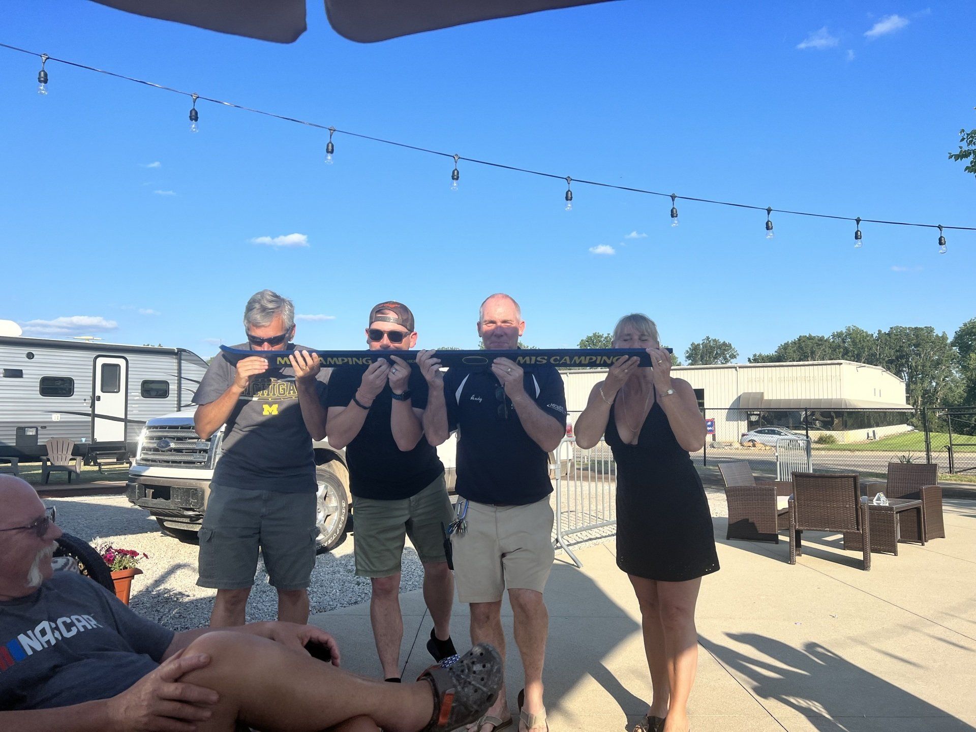 A group of people standing in front of a rv with a man laying on the ground