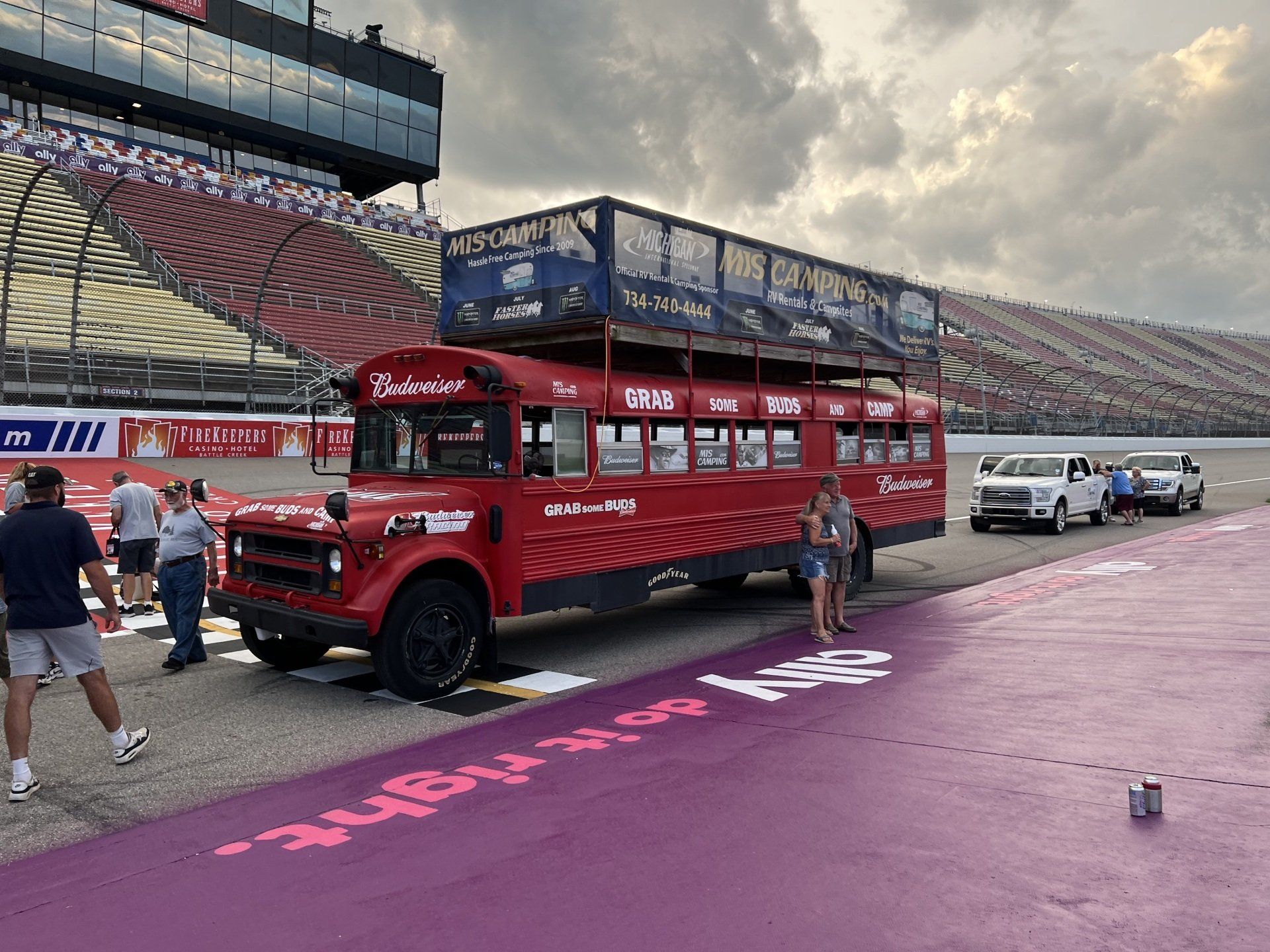 A red double decker bus is parked on the side of a race track.