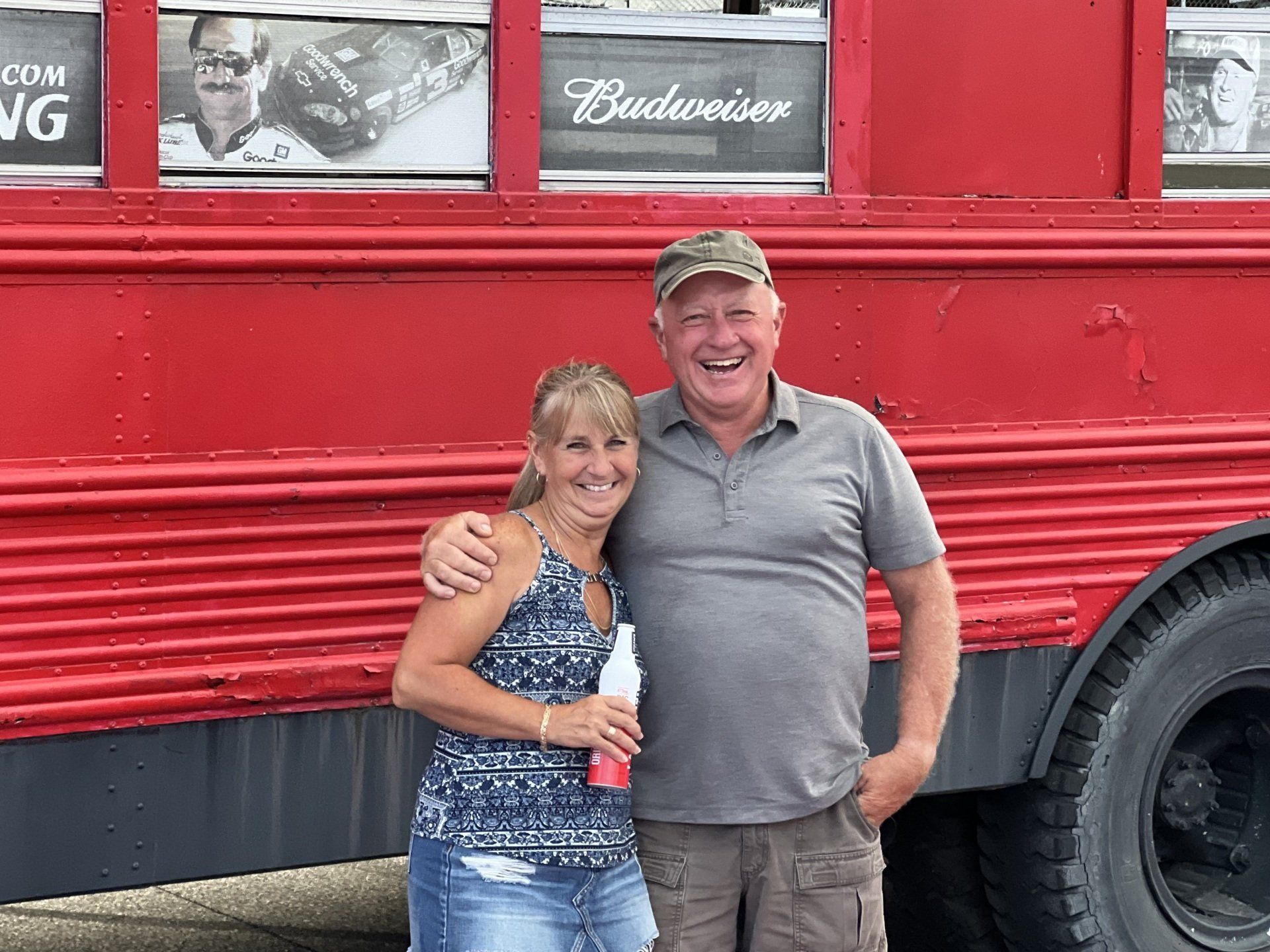 A man and a woman are posing for a picture in front of a red bus.