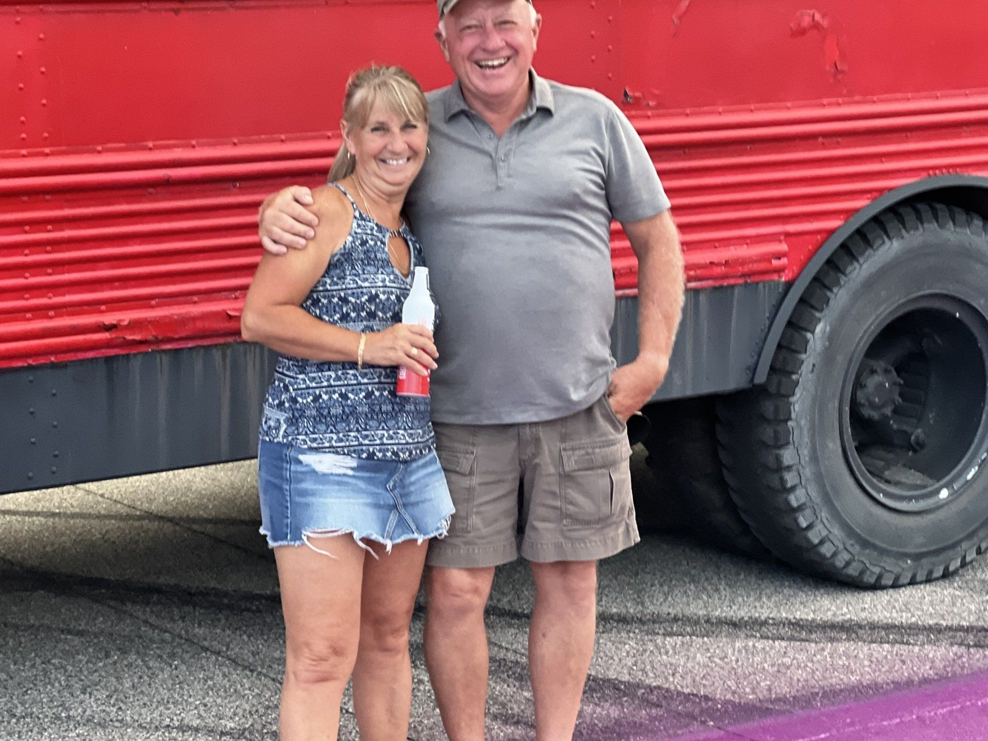 A man and a woman are posing for a picture in front of a red bus.
