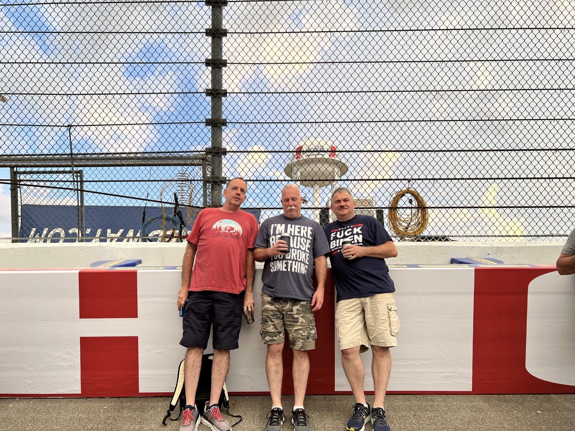 Three men are standing next to each other in front of a fence.