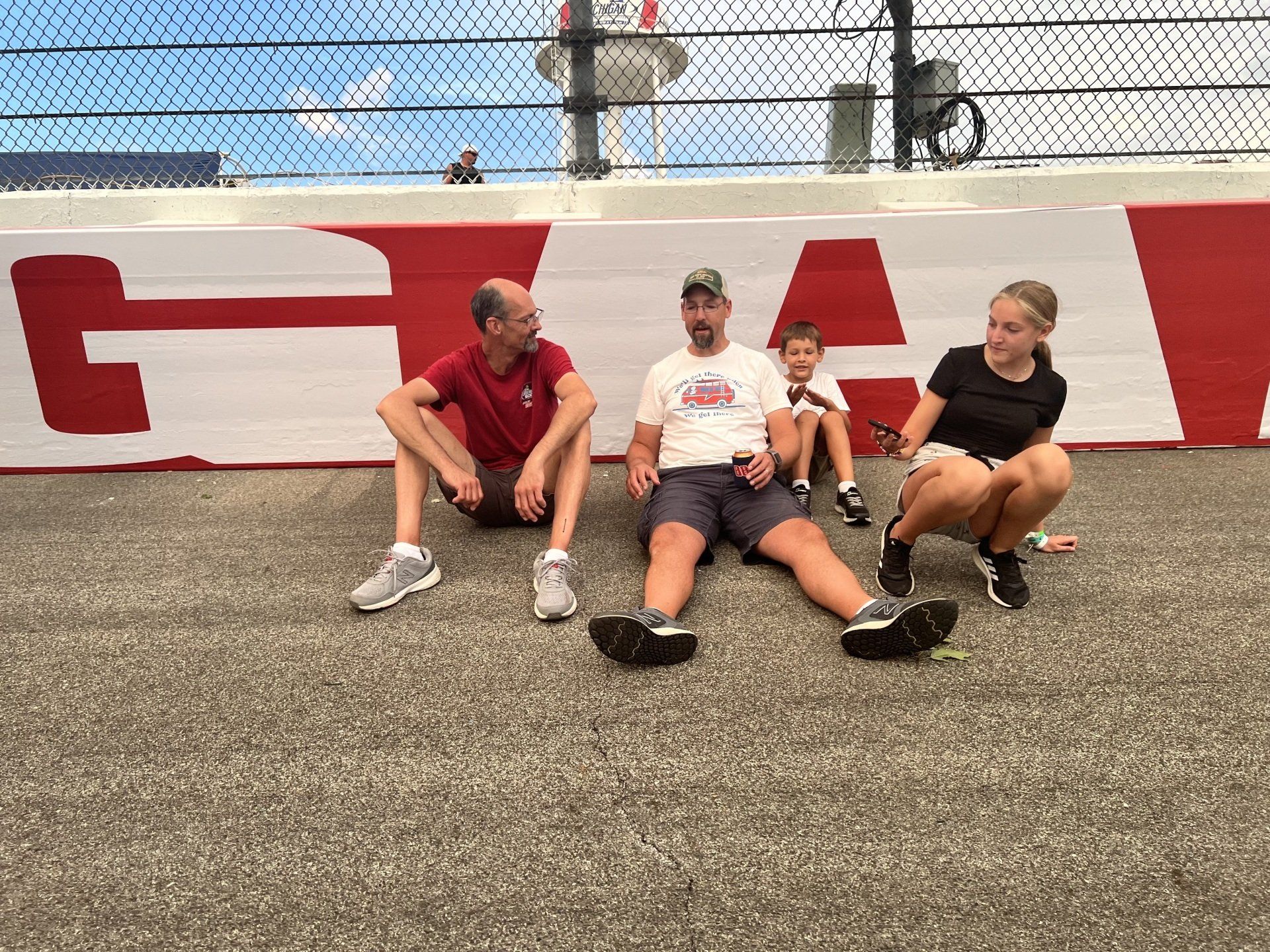 A group of people are sitting on the ground in front of a wall with the letter g on it