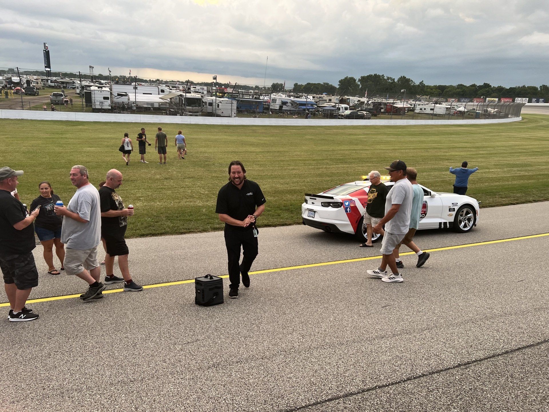 A group of people are walking down a road next to a race car