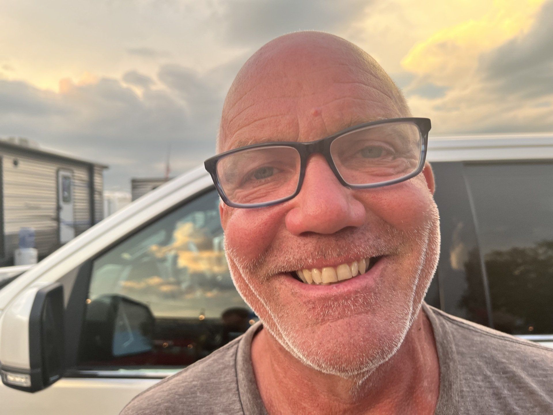 A man wearing glasses is smiling in front of a white van
