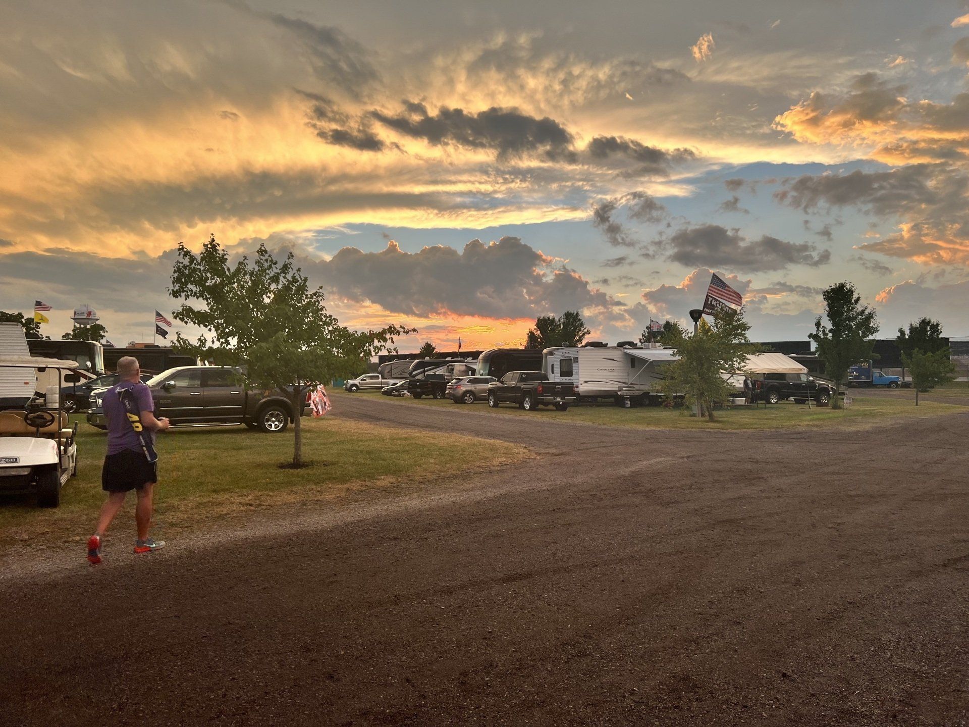 A man is walking down a dirt road in a park at sunset.