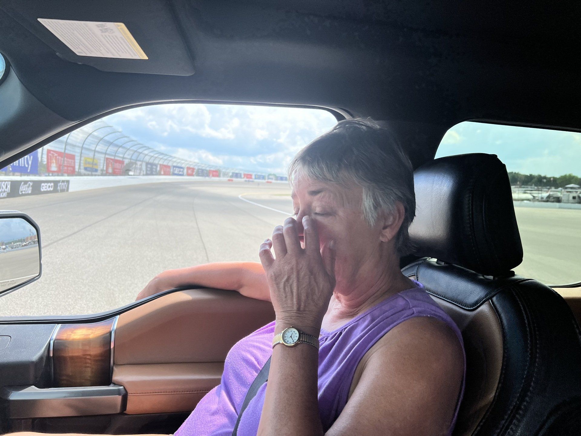 A woman is sitting in the driver 's seat of a car covering her nose
