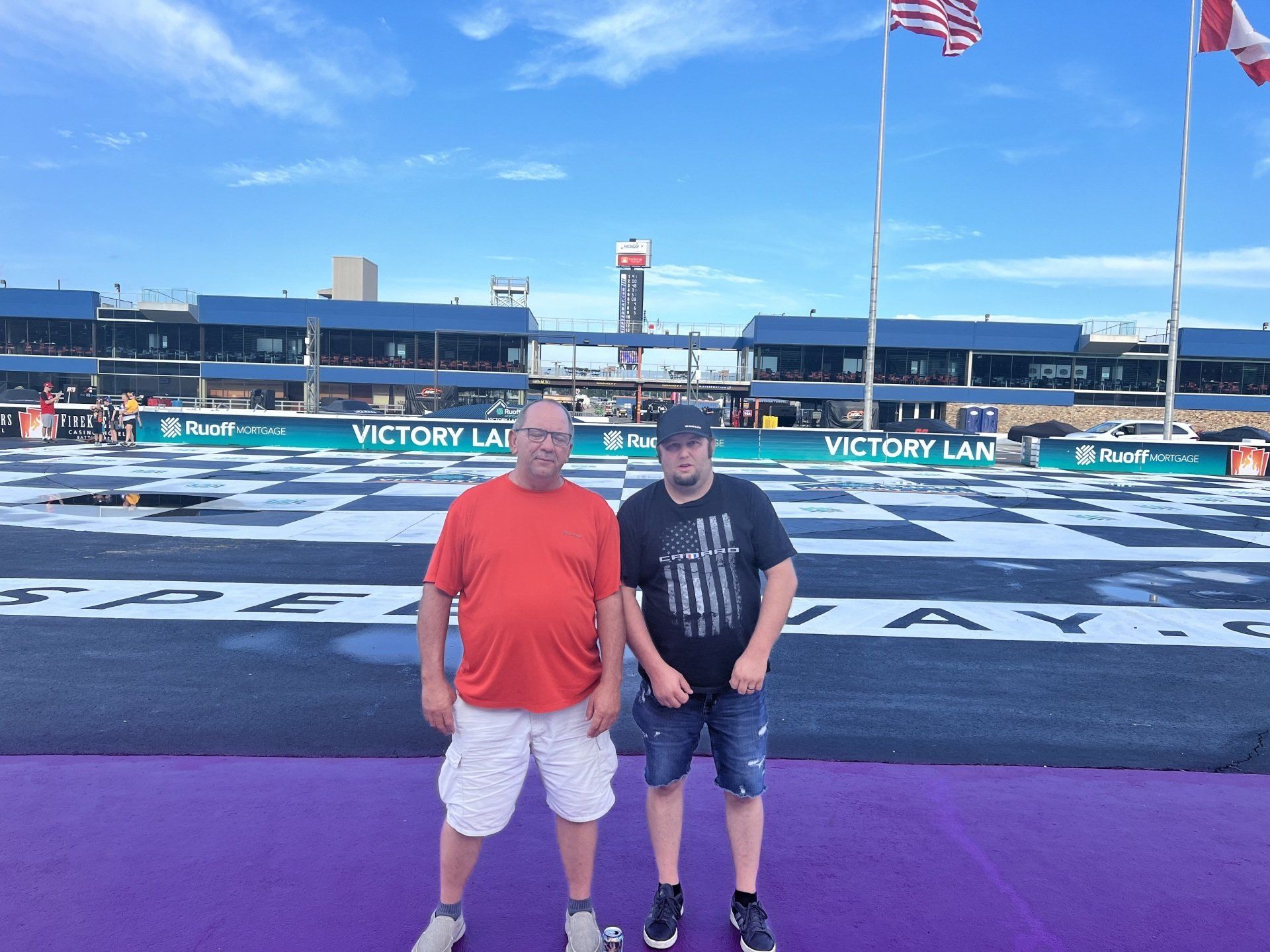 Two men standing in front of a race track that says victory lane