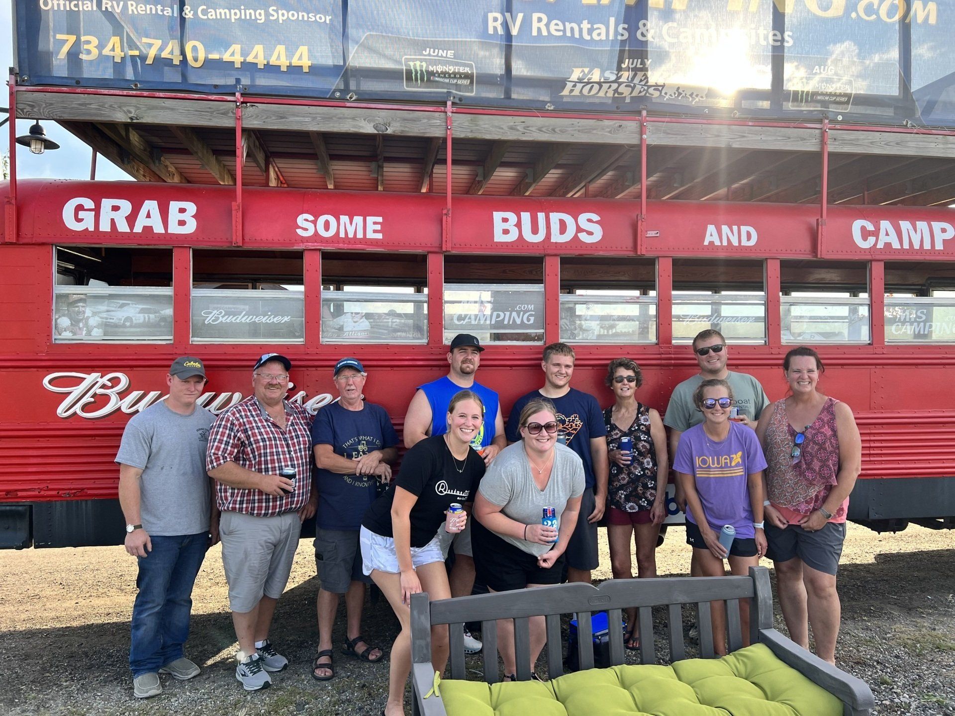 A group of people standing in front of a red bus that says grab some buds and camp