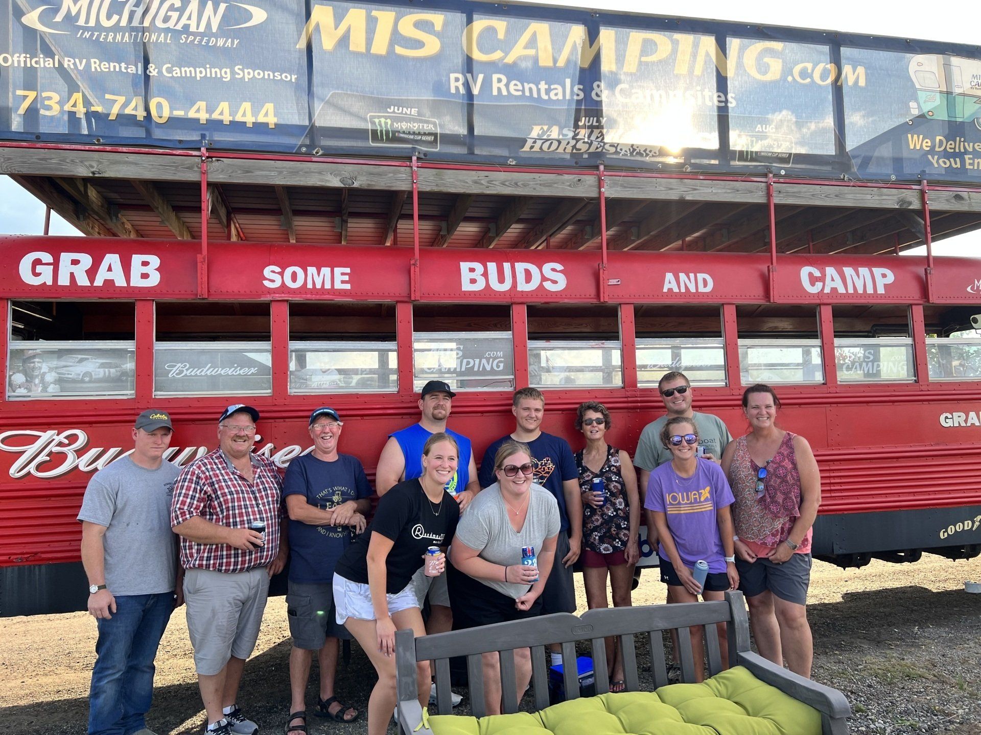 A group of people standing in front of a red bus that says grab some buds and camp
