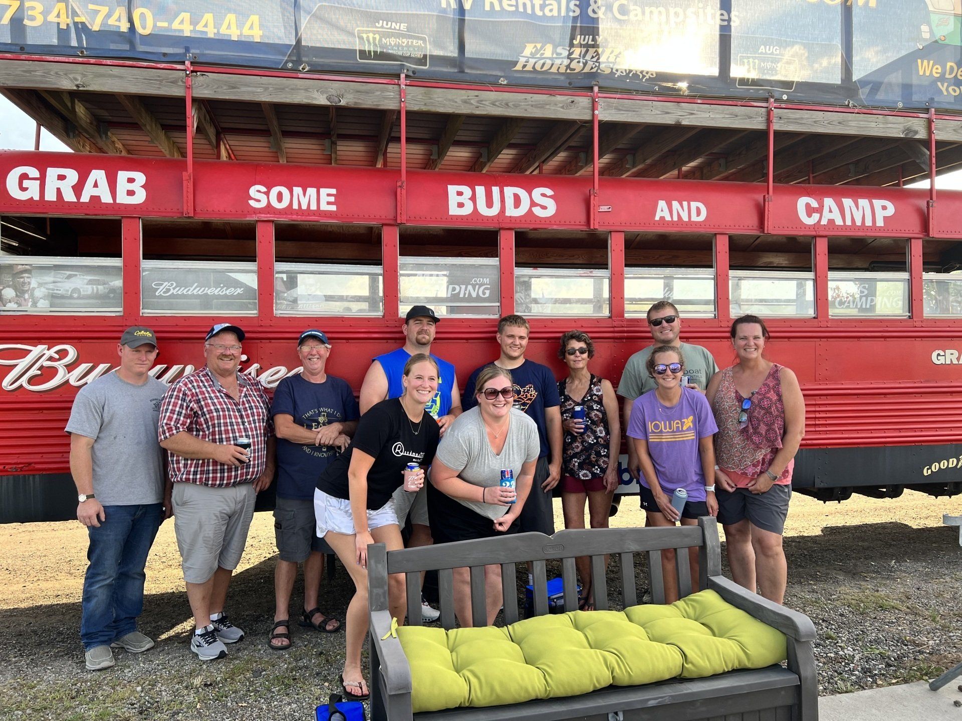 A group of people standing in front of a red bus that says grab some buds and camp