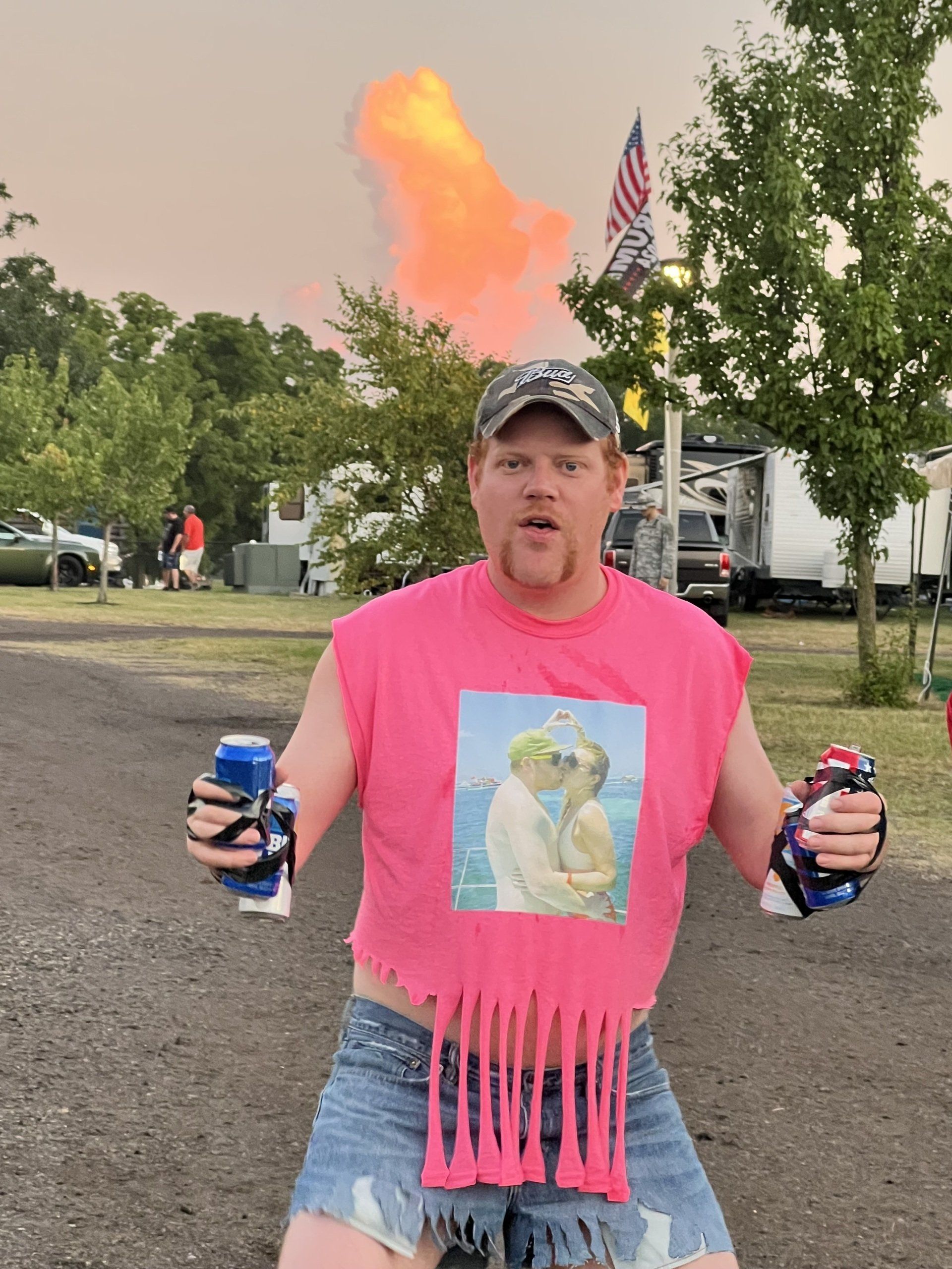 A man in a pink shirt is holding two cans of soda