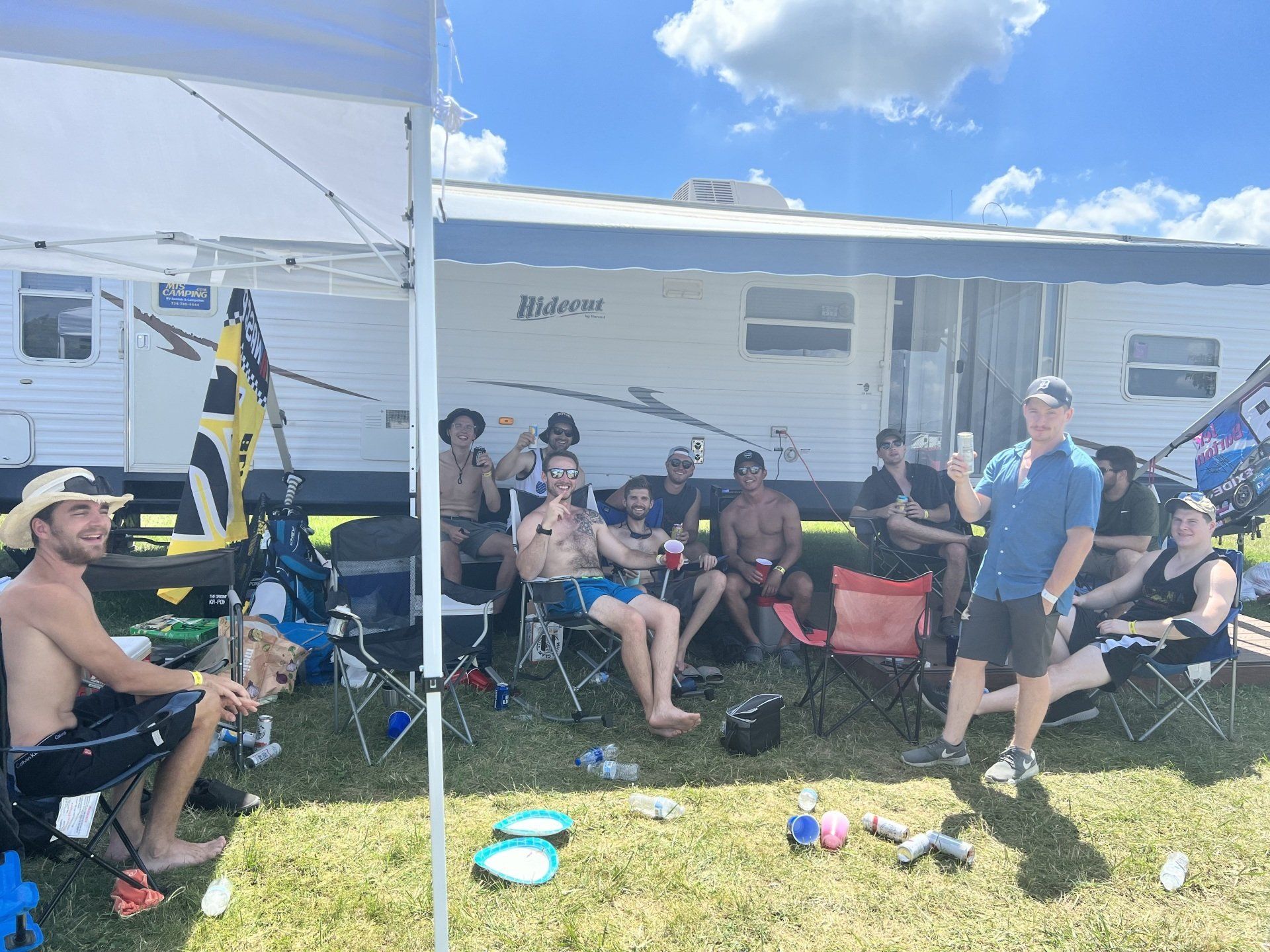 A group of people are sitting under a tent in front of a trailer.