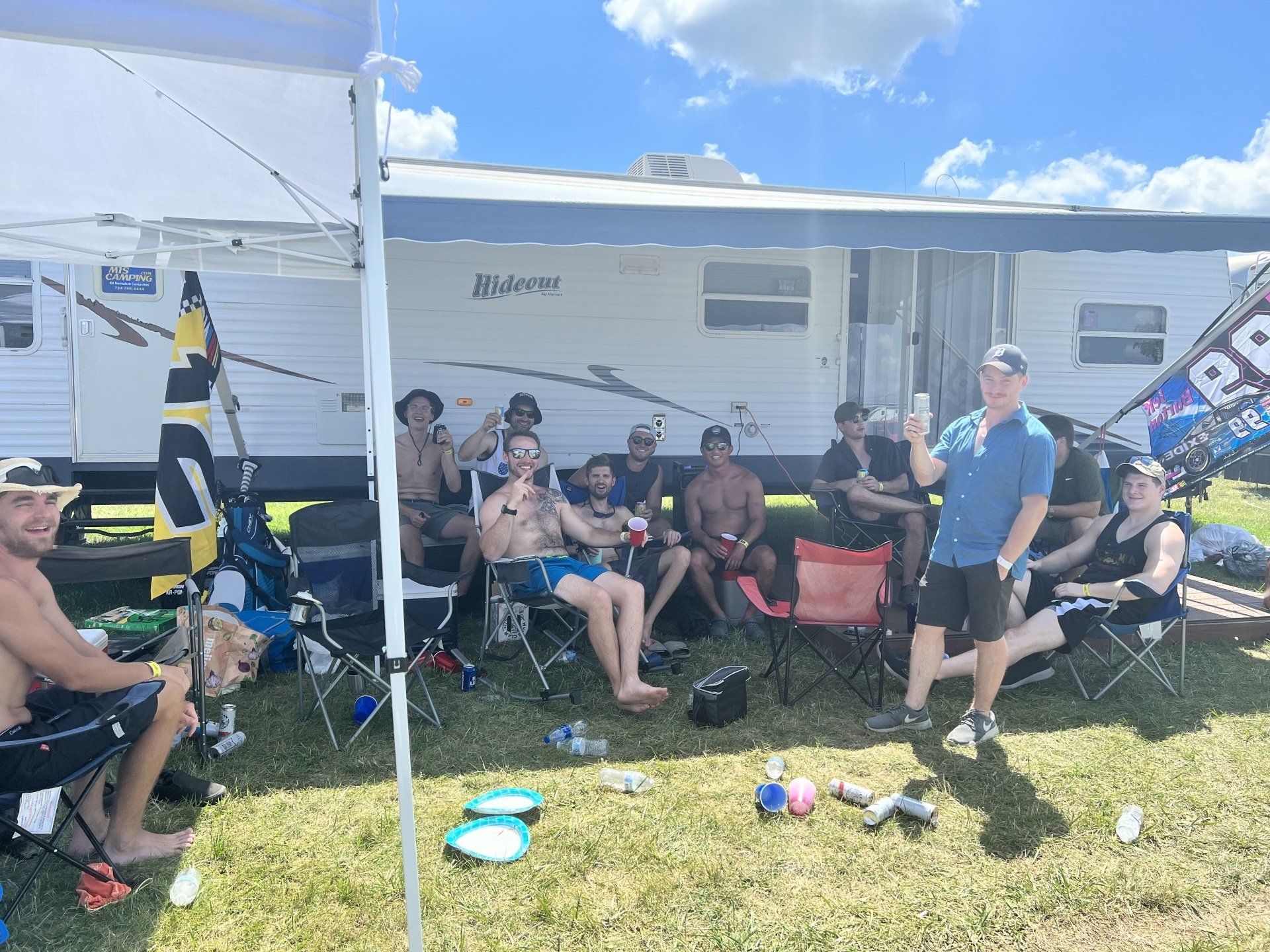 A group of people are sitting under a tent in front of a rv.
