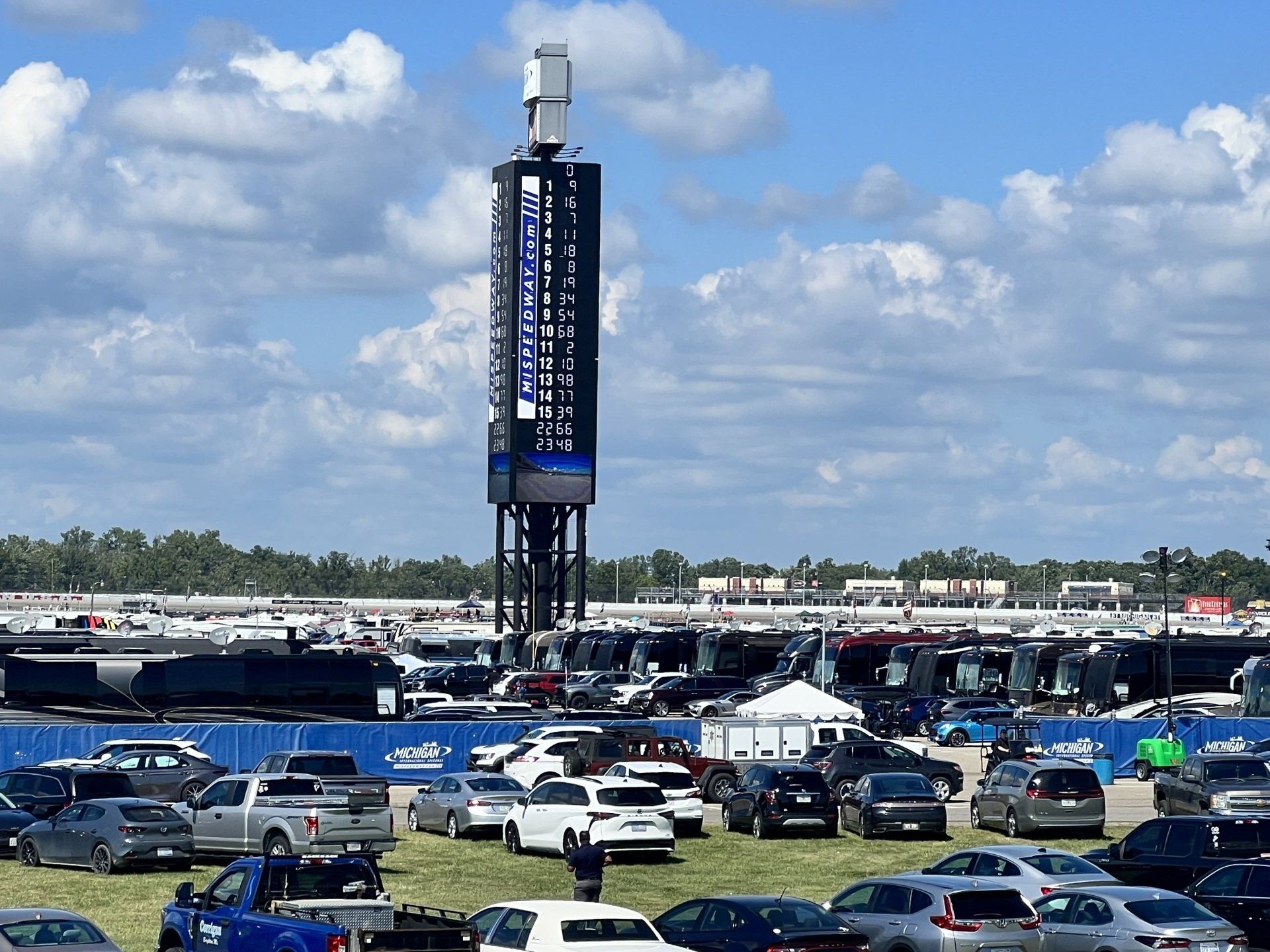 A lot of cars are parked in a parking lot with a scoreboard in the background