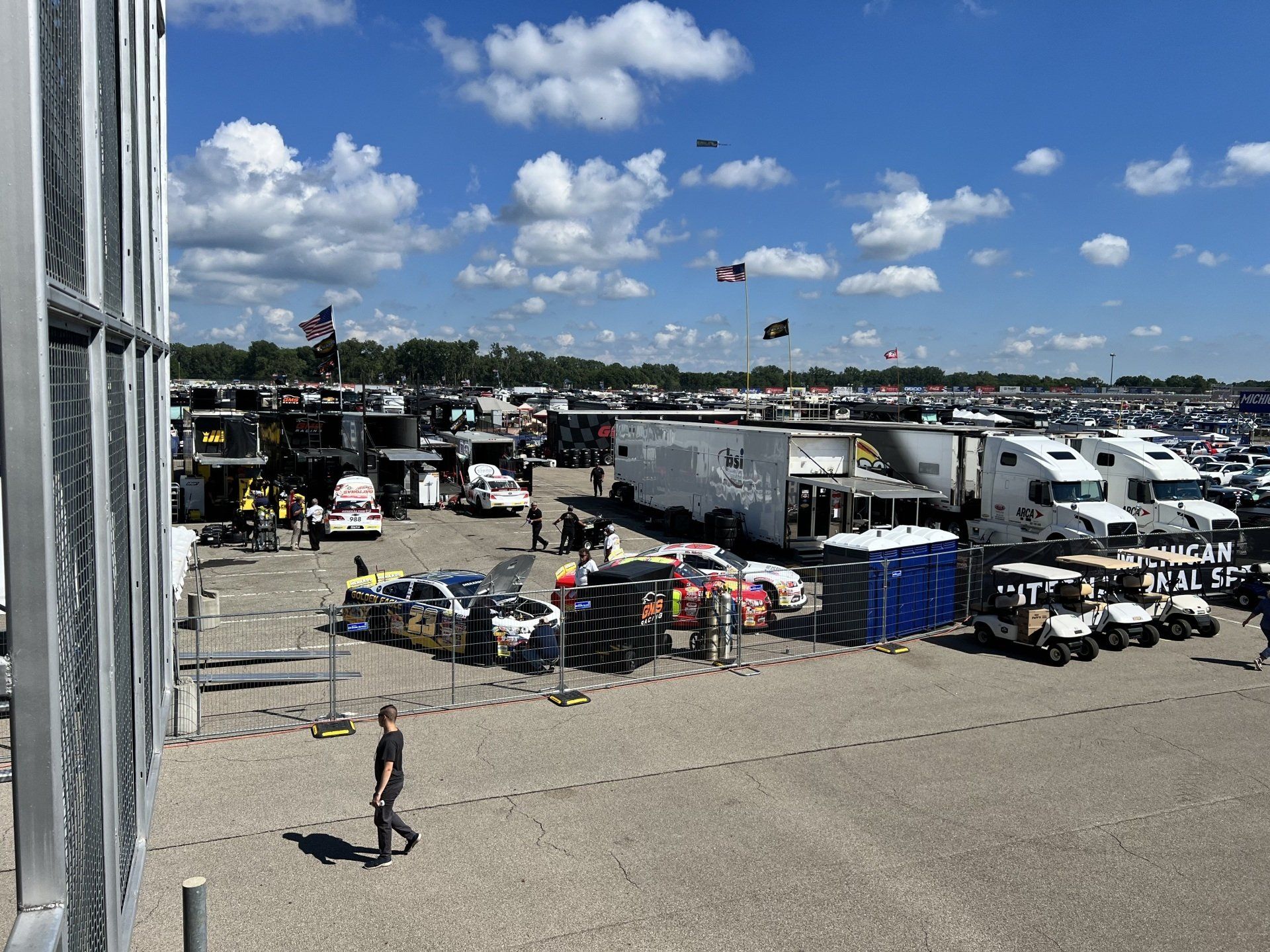 A man is walking through a parking lot filled with cars and trucks.