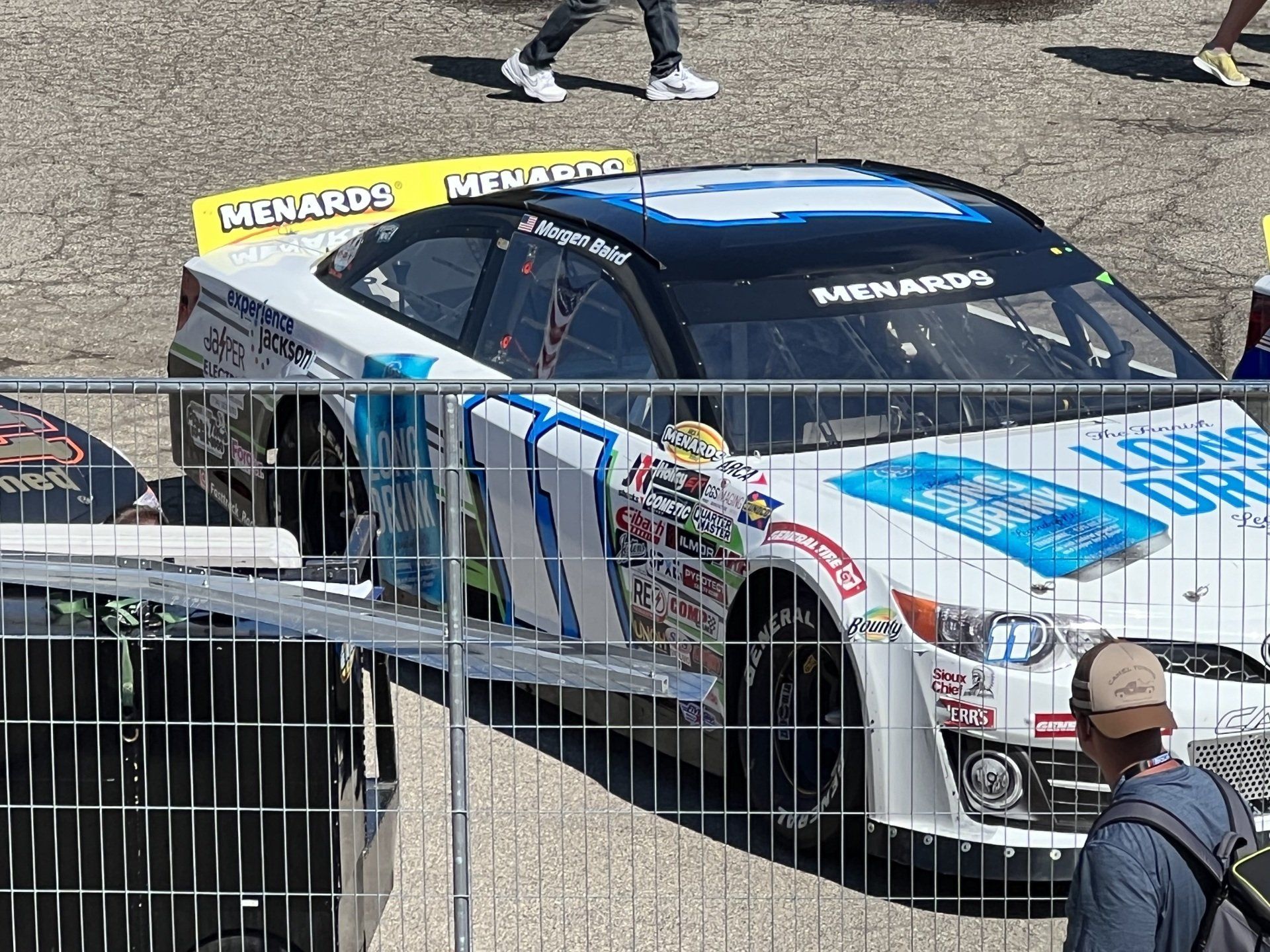 A race car is parked behind a fence with menards on the side