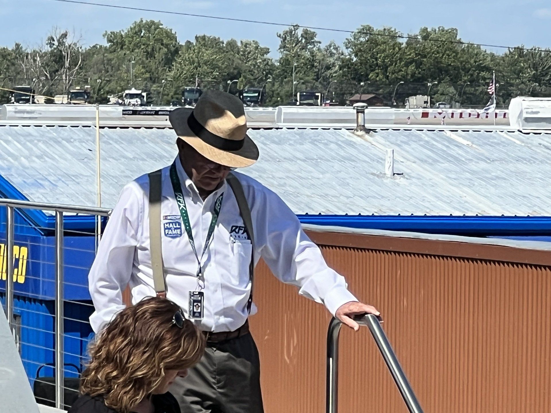 A man wearing a hat and suspenders is talking to a woman