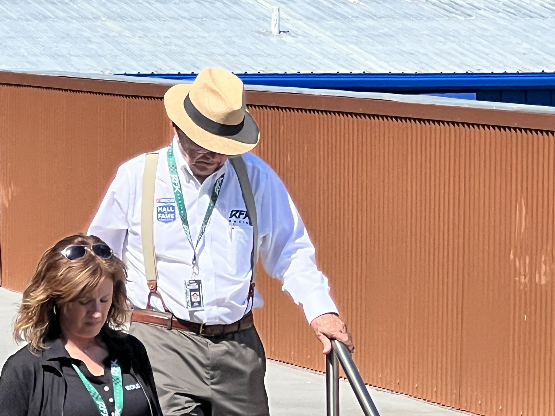 A man wearing a hat and suspenders is walking with a woman