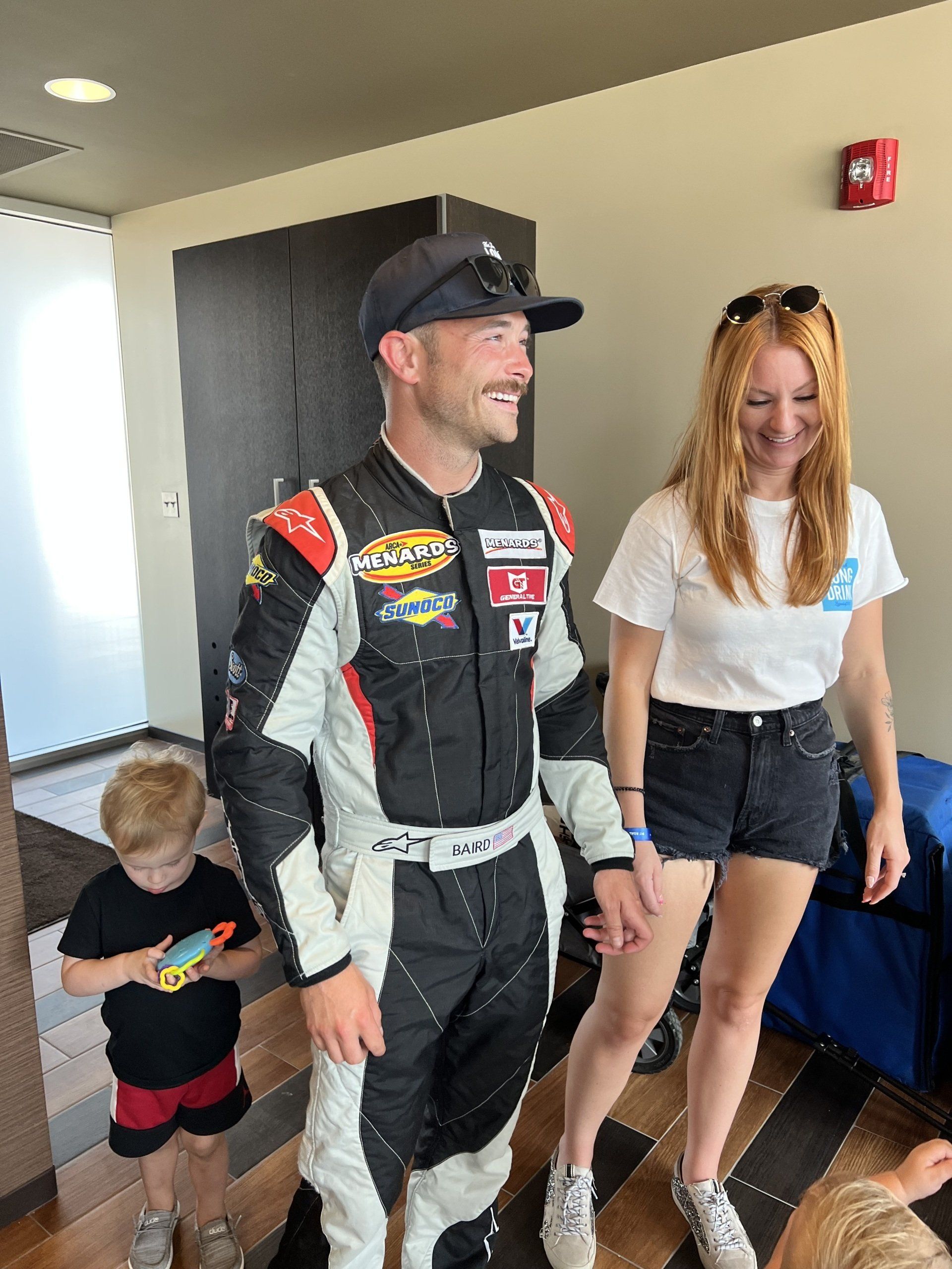 A man in a racing suit is standing next to a woman and a child.