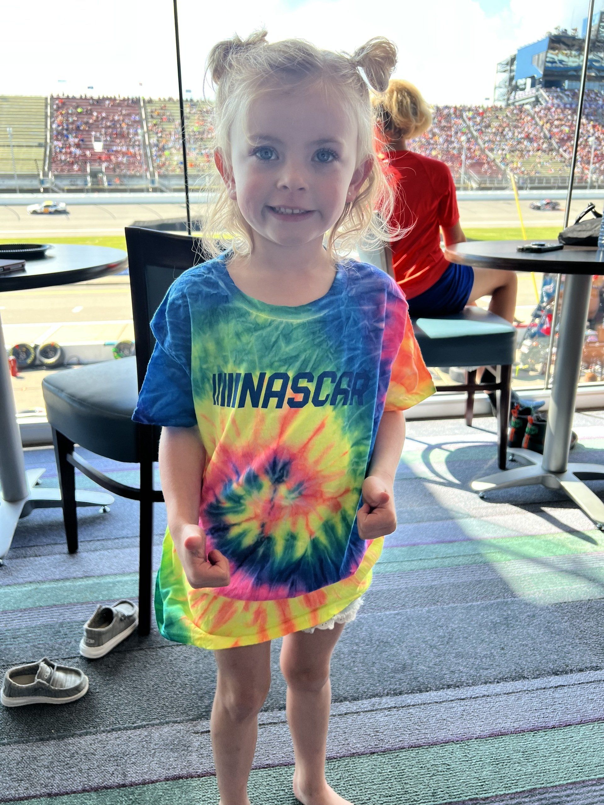 A little girl wearing a tie dye shirt that says nascar